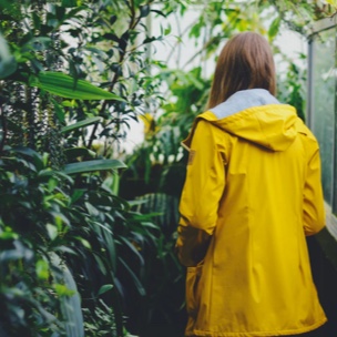 Girl in yellow jacket with her back toward the viewer, looking at plants.