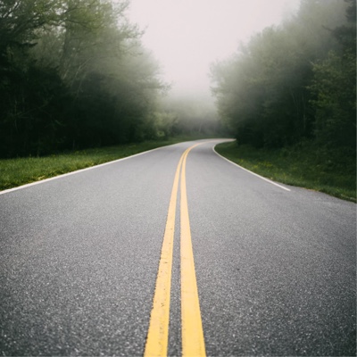 Paved road with a double yellow line in the center. There are trees on both sides of the road and fog in the distance.